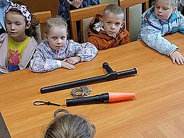 dzieci siedzą przy stole i oglądaja pałkę policyjną
