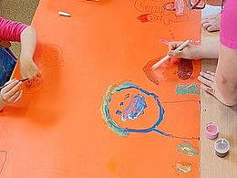 dzieci malują farbami na pomarańczowym kartonie