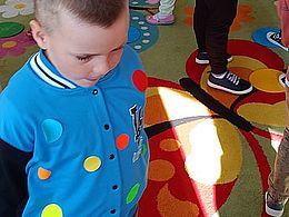 Dzieci ubrane w kropki chodzą po dywanie, na którym rozrzucone są kropki 