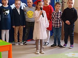 Dziewczynka stoi z mikrofonem, za nią dzieci stoją w rzędzie 
