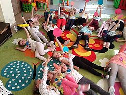 Dzieci leżące na dywanie i trzymające kropki w wyciągniętych przed sobą rękach