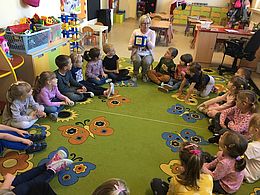 dzieci siedzą w kółku i obserwują nauczycielkę trzymającą kostkę z emocjami
