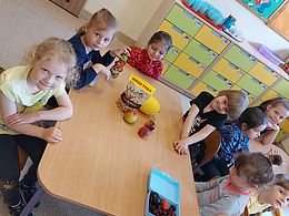 Dzieci siedzą przy stoliku i zjadają owoce