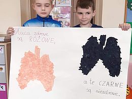 Chłopcy trzymają plakat z płucami: zdrowym i zniszczonym przez palenie papierosów 