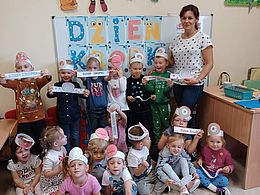 Dzieci i nauczycielka w kolorowych opaskach na głowach pokazują napisy Dzień Kropki