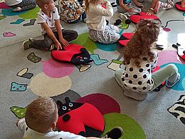 Dzieci siedzą na dywanie i przyczepiają rzepami kropki do materiałowych biedronek