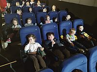 Dzieci siedzą na krzesełkach w sali kinowej 