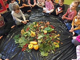 dary jesieni rozsypane na folii, wokół siedzą dzieci