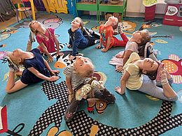 Dzieci wykonują skłony siedząc na podlody