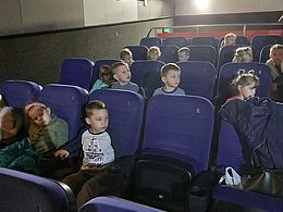 Dzieci siedzą na krzesełkach w sali kinowej 