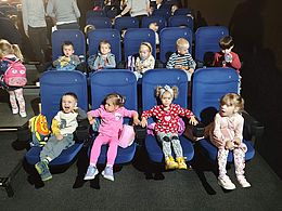 Dzieci siedzą na krzesełkach w sali kinowej