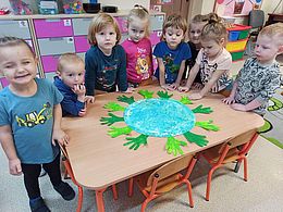 Dzieci wokół stolika na którym jest okrągły pomalowany na niebiesko i zielono karton 