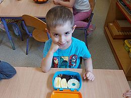 Chłopiec siedzi przy stoliku, podpiera głowę ręką i ma przed sobą kanapnik z owocami 