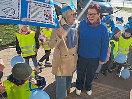 Dwie kobiety i dzieci na chodniku pozują do zdjęcia z niebieskimi emblematami