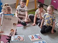 Dzieci siedzą w kole, w środku są kolorowe obrazki