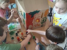 Dzieci mazakami ozdabiają kartonowe pudło