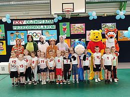 Dzieci w strojach sportowych pozują z maskotkami Olimpiady, postaciami z bajek 