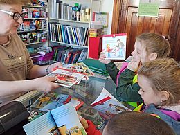 Dzieci razem ze sprzedawczynią przeglądają książki dla dzieci 